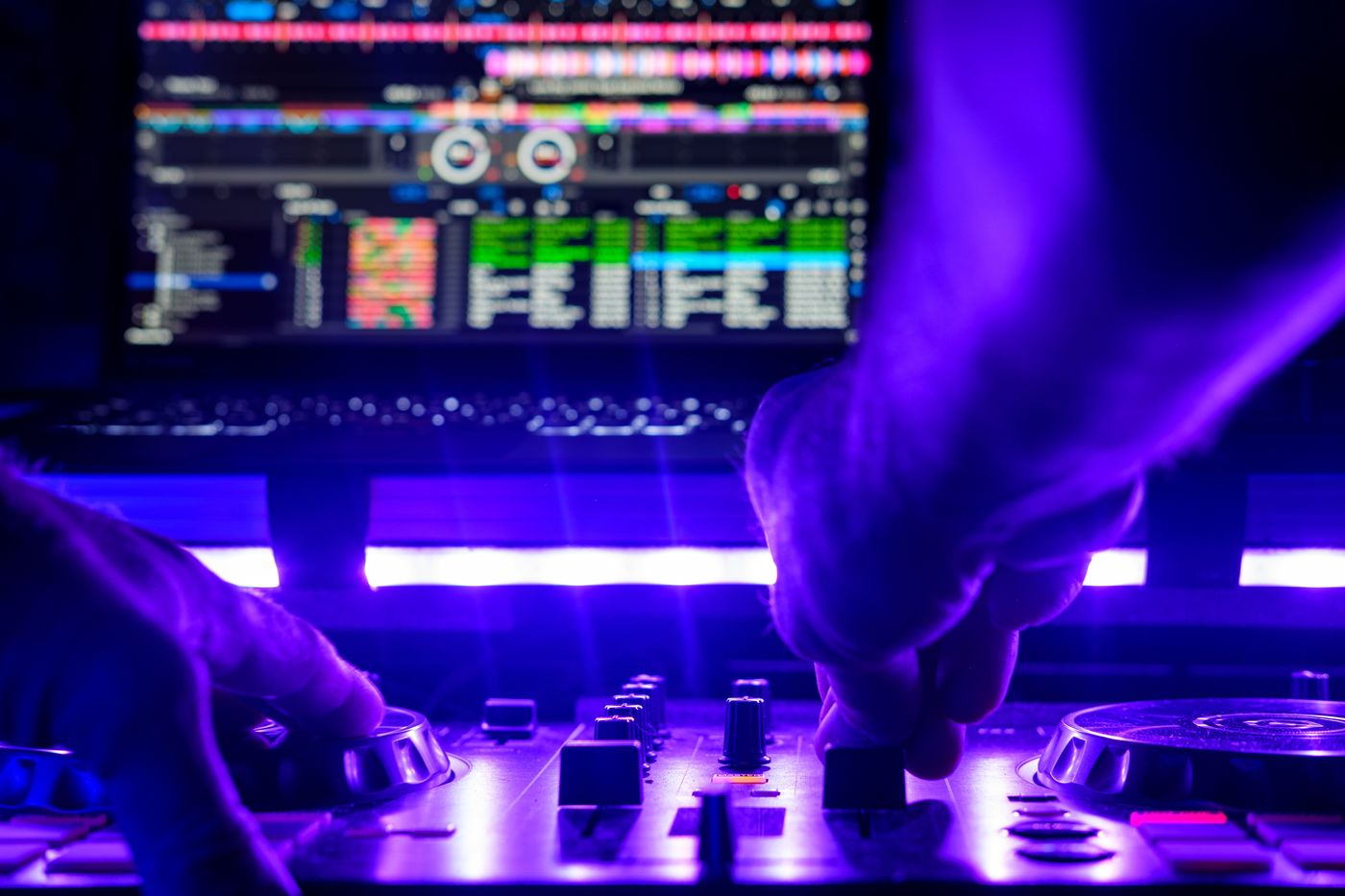 Hände von DJ Voltino am DJ-Mischpult im violetten Clublicht bei einem Event in München